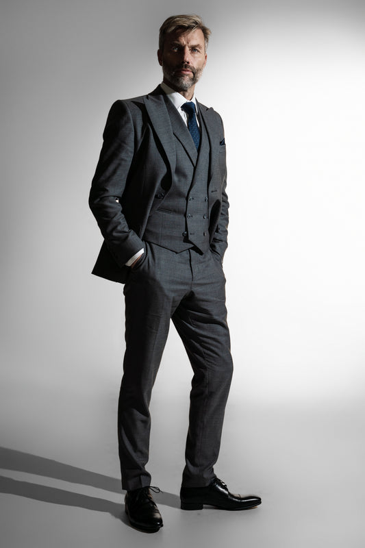 Fornem skægget mand i en mørkegrå tredelt skræddersyet jakkesæk, der ser selvsikkert frem mod en hvid baggrund