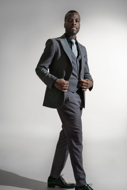 Selvsikker afroamerikansk mand i en kulgrå skræddersyet jakkesæk med en teal slips, stående mod en hvid baggrund