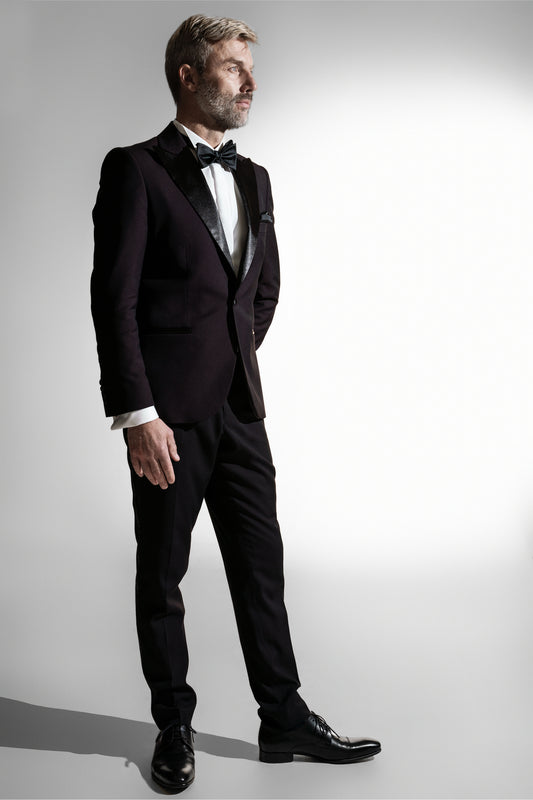 Sofistikeret mand i en dyb lilla smoking med en sort butterfly, der poserer mod en lys grå baggrund