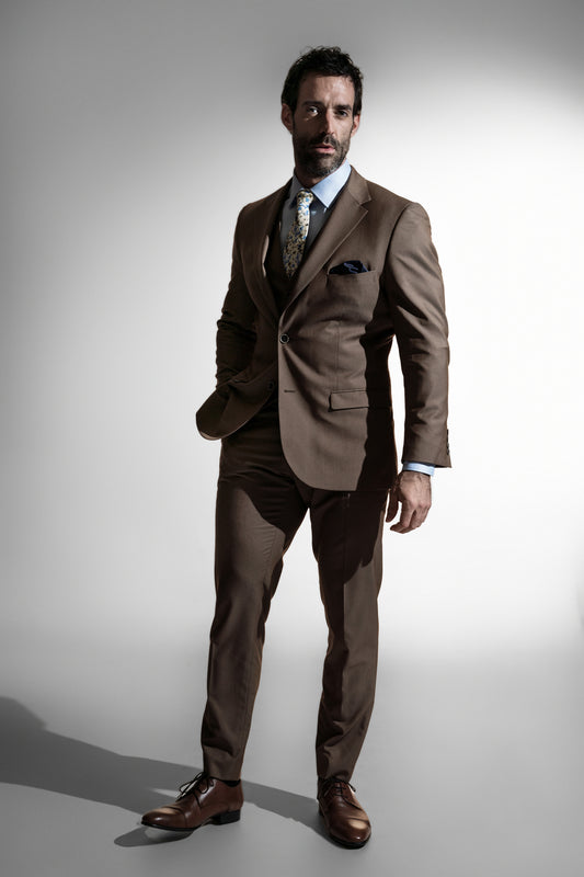 Attraktiv mand i et brun skræddersyet jakkesæk med et blomstret slips og lommetørklæde, der står selvsikkert mod en neutral baggrund