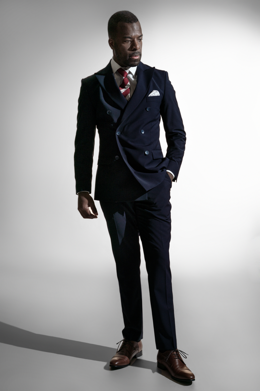 Fornem mand i en marineblå dobbeltradet skræddersyet jakkesæk med et stribet slips, står velafbalanceret mod en lys baggrund