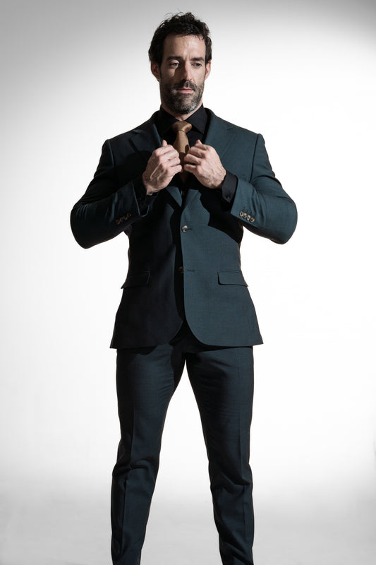 Elegant mand justerer sit brune slips, iført en mørk teal suit  sat mod en lys baggrund