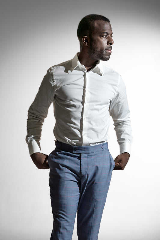 Tankefuld afroamerikansk mand i en hvid skjorte og mønstrede blå bukser, poserer mod en hvid indstilling