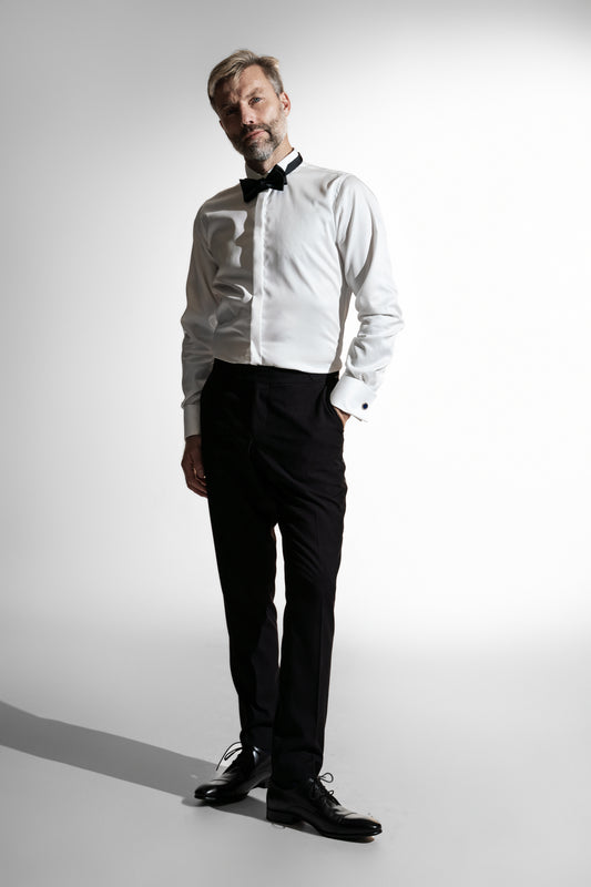 Mand i en klassisk hvid skjorte med sort butterfly, matchet med sorte bukser, der fremviser et formelt look mod en lys indstilling