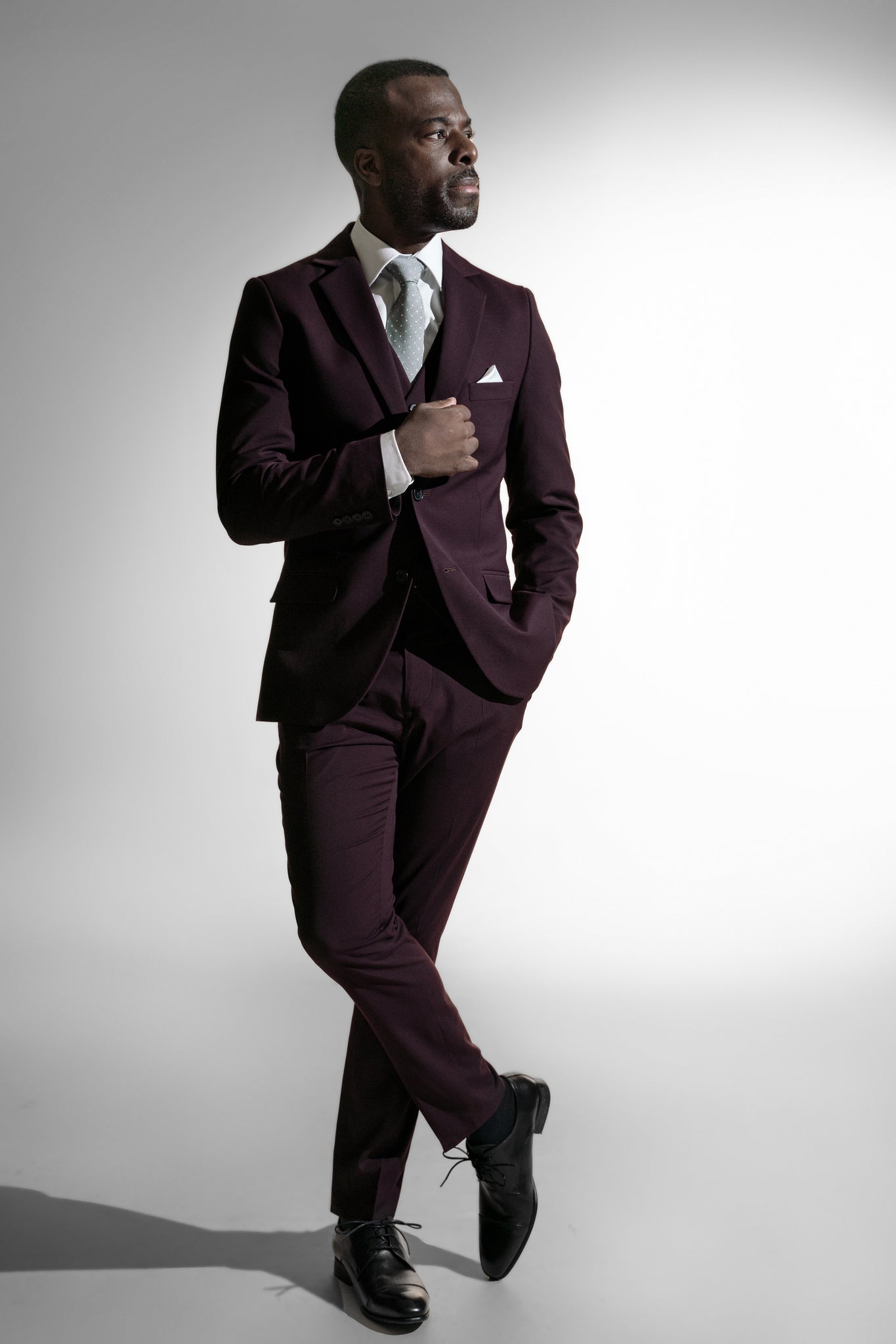 Elegant afroamerikansk mand i maroon skræddersyet jakkesæk, der holder sin jakkes revers mod en hvid baggrund