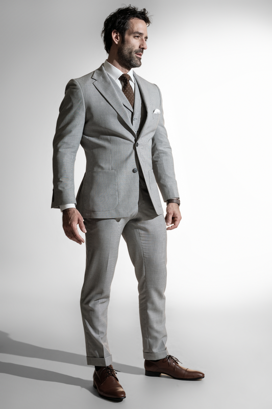 Stilfuld mand med mørkt hår i en lys grå skræddersyet jakkesæk parret med en brun slips, stående mod en hvid baggrund