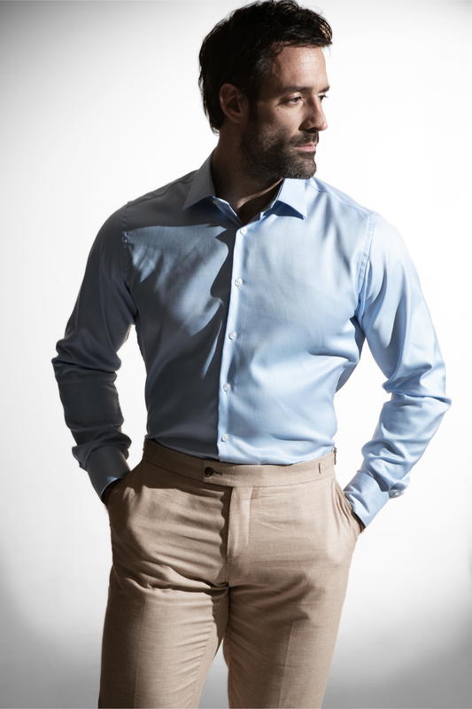 Selvsikker mand i en lyseblå skjorte parret med beige bukser mod en lysende baggrund