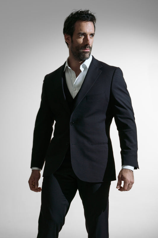 Elegant mand i en skræddersyet sort skræddersyet jakkesæk med en hvid skjorte, ser eftertænksom ud